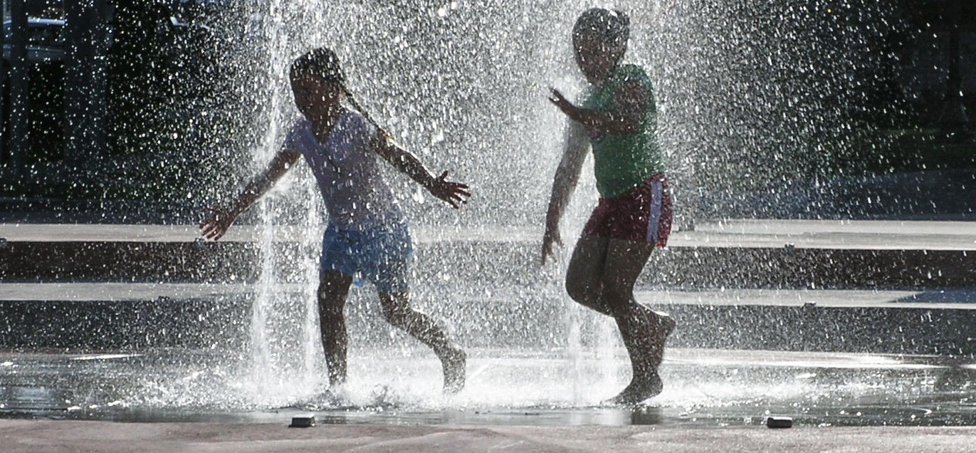 Children play outdoors in water fountain.